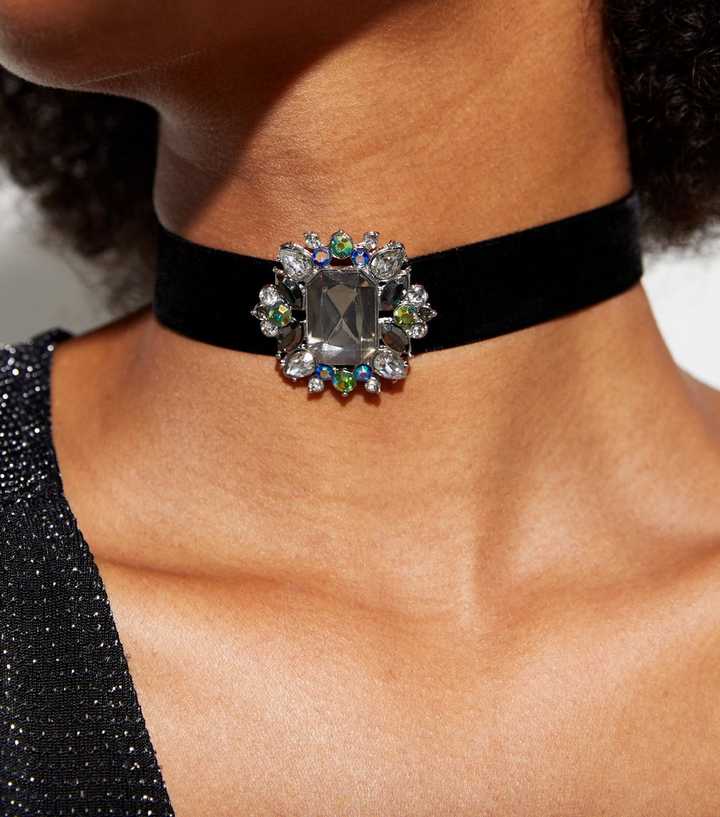 An opulent gemstone pendant choker on a black velvet band gracefully encircles the neck of a woman, its large central stone surrounded by a halo of multicoloured gems catching the light with every movement. This piece is a blend of vintage glamour and contemporary style, adding a touch of luxury and a dash of boldness to any ensemble.